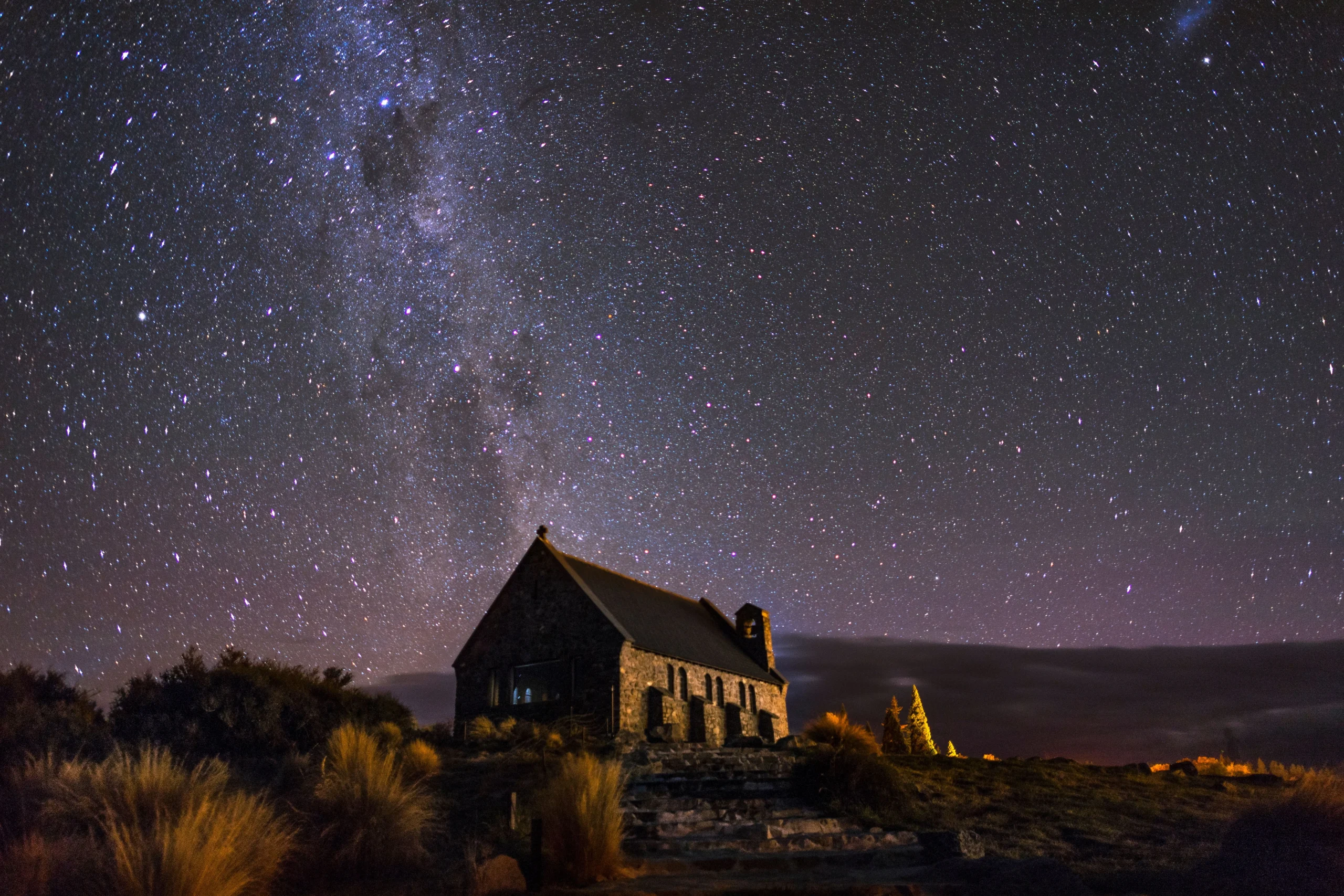 Historic stone church illuminated at night alongside a lake, framed by the Milky Way galaxy.