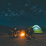 People sitting around a campfire as smoke drifts toward them