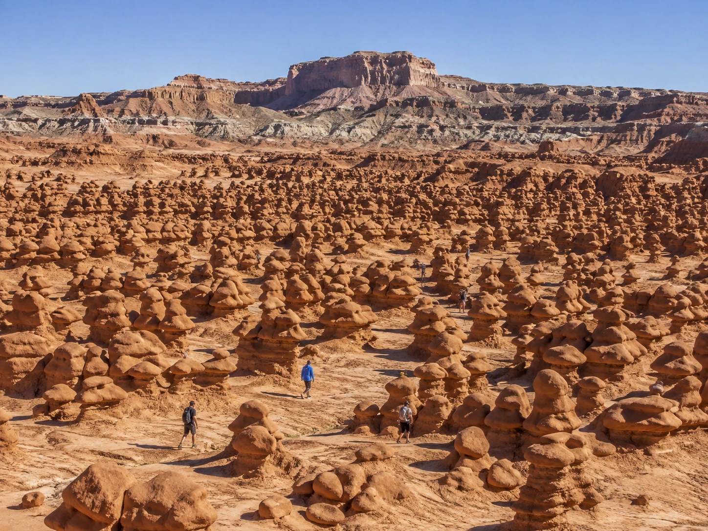 Visitors walking among sandstone hoodoos in the Valley of the Goblins