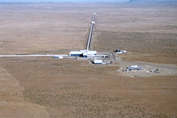 Aerial view of an L-shaped gravitational-wave detector with two four-kilometre interferometer arms extending at a right angle across a desert landscape.