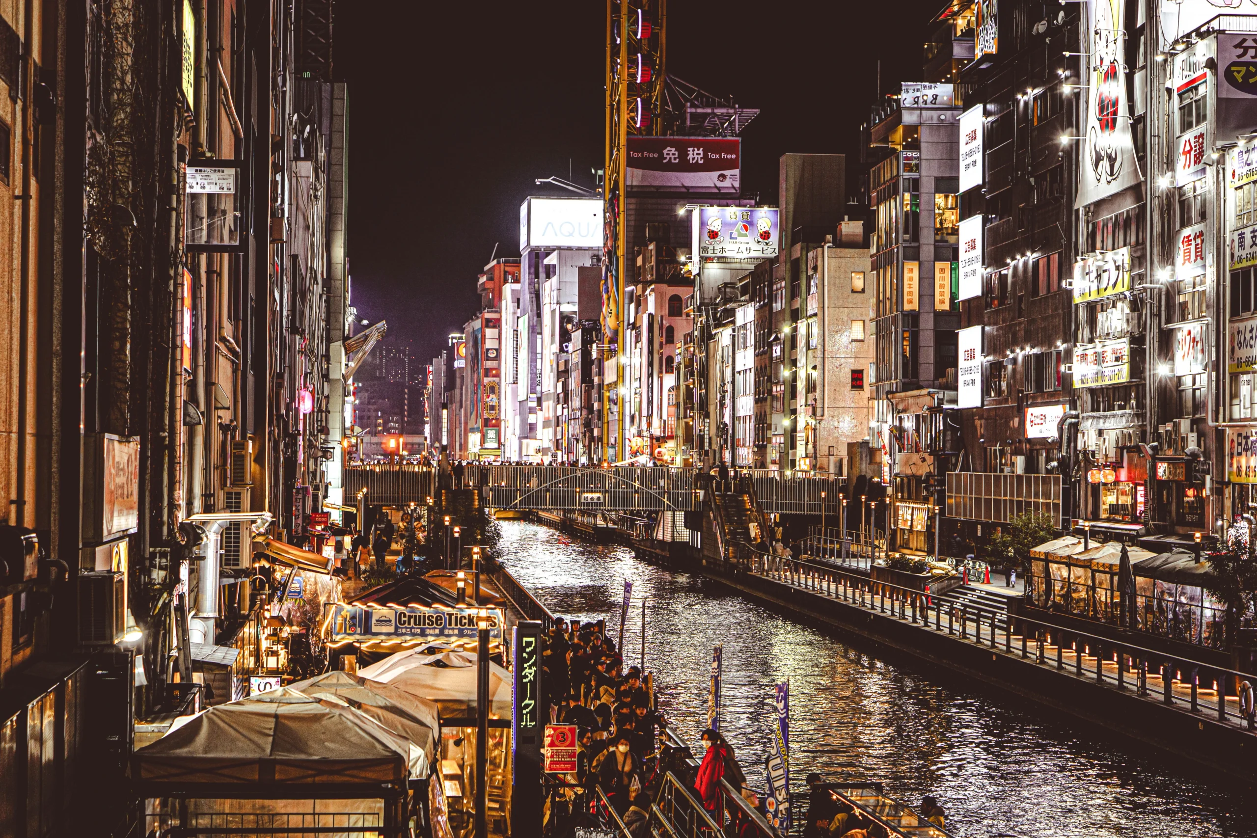Illuminated signs and waterfront restaurants reflected in Osaka’s Dotonbori canal at night.